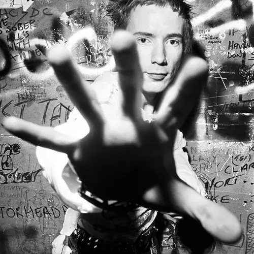 Black and white photograph of Johnny Rotten posing with his hand outstretched towards the camera.