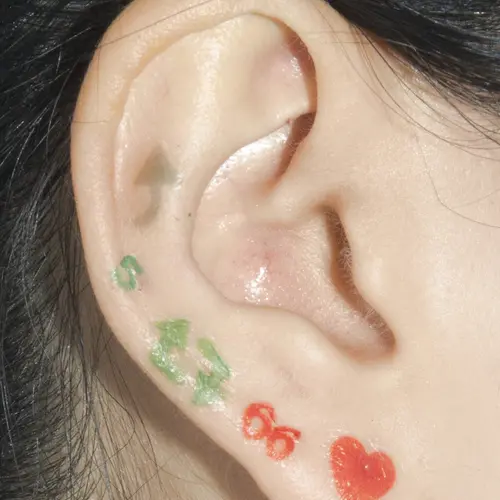 Close-up photograph of John Yuyi's ear with social media stickers