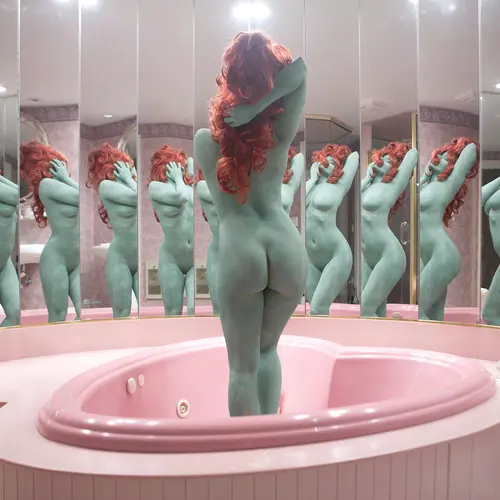 A nude woman with skin painted in a pale teal colour and bright copper-coloured hair obscuring her face, stands in the middle of an empty, pink, heart-shaped bath tub surrounded by a mirrored wall.
