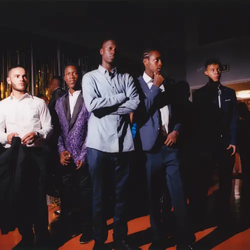 A group of young black men dressed in smart attire stood in a dark room.