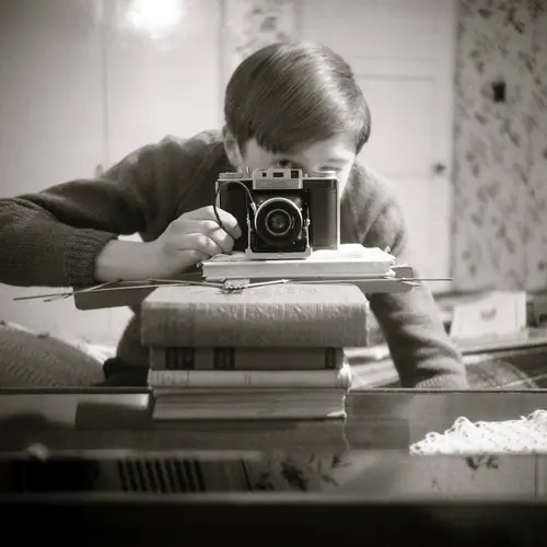 Black and white photograph of a person balancing a camera on a pile of books.
