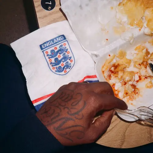 Colour image showing a person's hand next to some fish and chips and an England football logo on a napkin