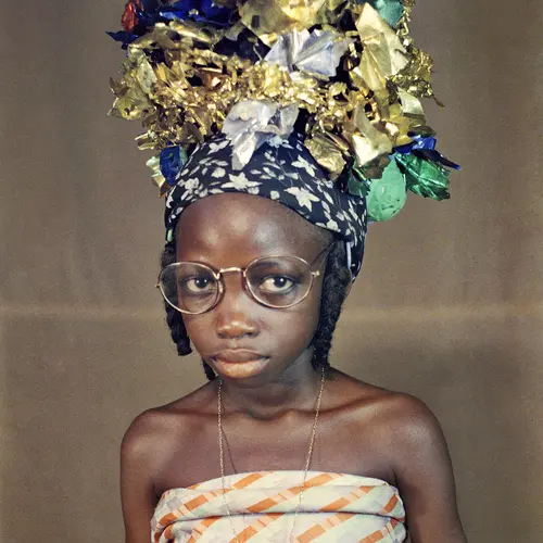 A young girl wearing large glasses and a colourful metallic headwrap in a photography studio.