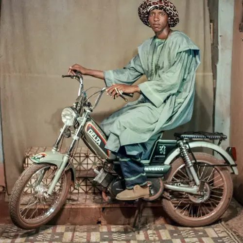 Colour photograph of a person posing on a motorbike.