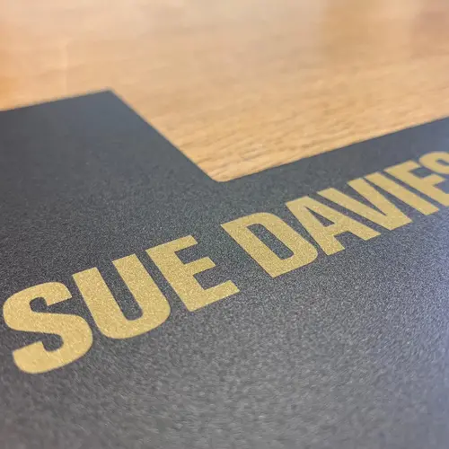 A close up of a black plaque with 'Sue Davies' written in gold