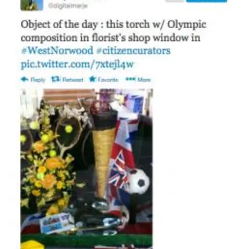 A tweet by Marjory Often  "Objet of the day:  this torch w/ Olympic composition in florist's shop window in #Westnorwood #citizencurators" A photograph of a tennis racket and a golden torch in a shop window 