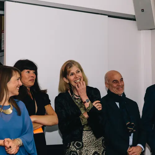 Group photograph of five people, standing in a room, watching something on the other side of the room