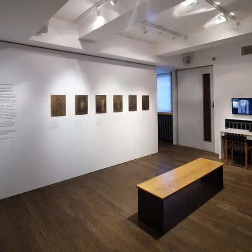 A room with prints along one wall and a screen on another, with a museum bench in the middle