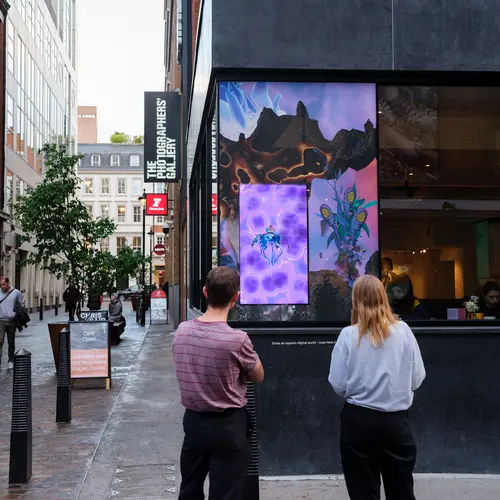 Two people watch an animation of a jellyfish, which is on a screen in a window surrounded by a colourful print 