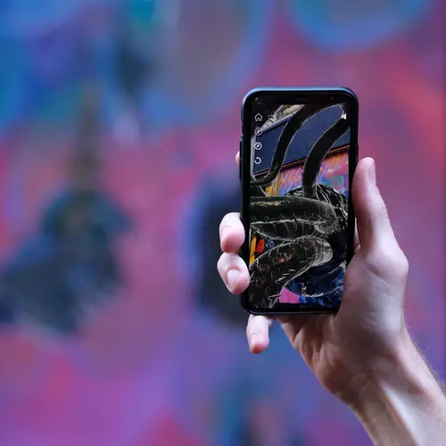 A hand holds an iphone that shows 3D tentacles on a real world environment
