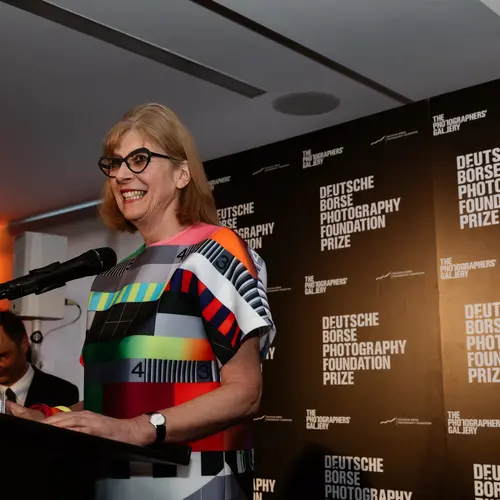 Group photograph of five people, standing in a room, watching something on the other side of the room