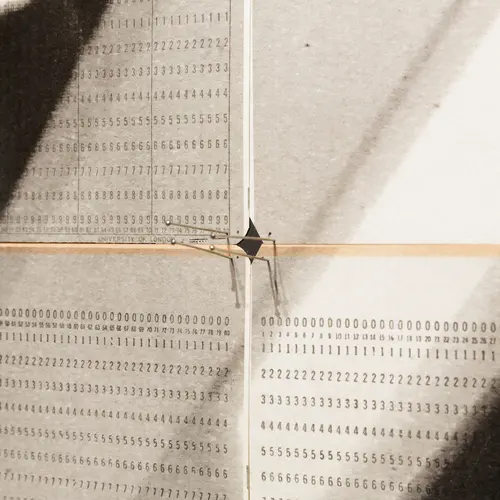 Close up of artwork showing pins, computer cards printed with black and white shapes and rows of numbers.