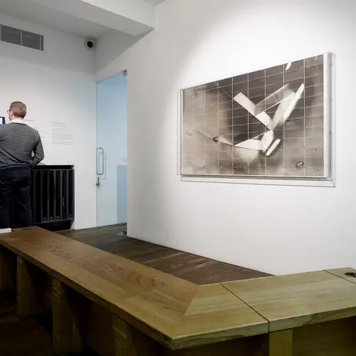 Room with wooden bench in front of framed artwork and person posting card in a wooden box.