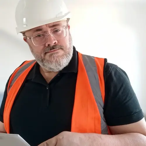A portrait of the artist wearing a white hard hat and a flourescent orange vest on top of a black shirt.