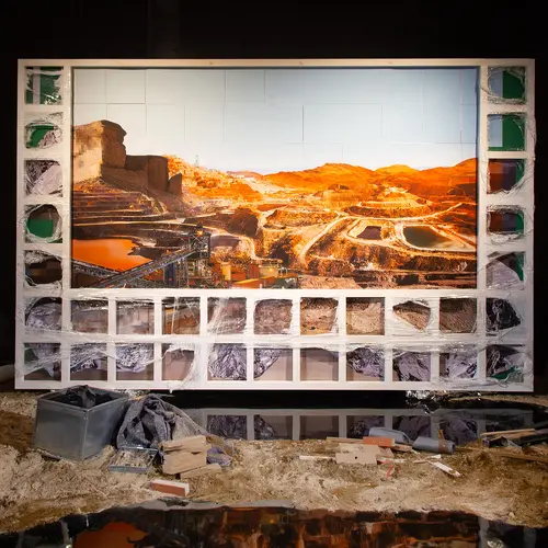 An install shot from the Felicity Hammond V3 Model Collapse exhibition. A large framed image of a red, arid landscape stands amongst sand, dirt, bricks and other rubble.