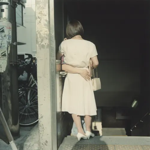 Colour photograph of the back of a woman standing against a wall. An arm can be seen around her waist.