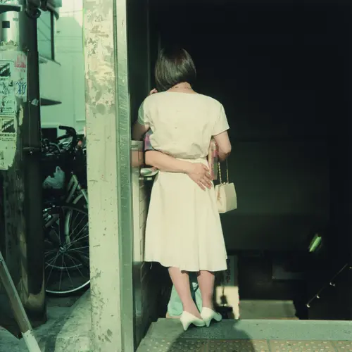 A vintage photo of the back of a woman in a white dress being wrapped in a hug by a set of arms.