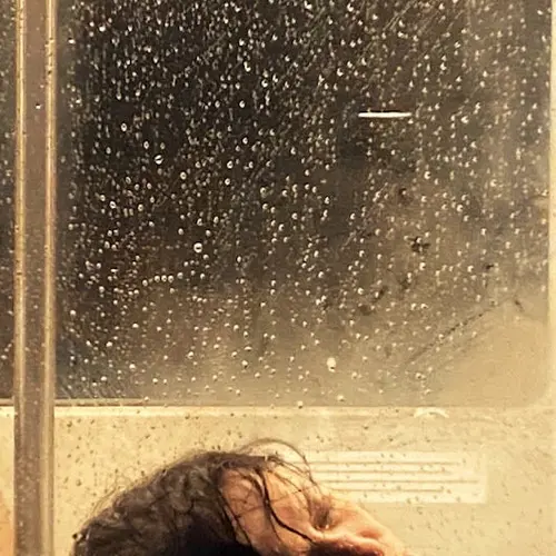 A photograph of a person laying their head against a glass window covered in condensation