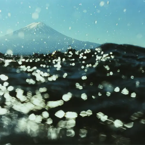A hazy image shot from just above the waves of the sea. Mount Fuji is visible on the horizon.