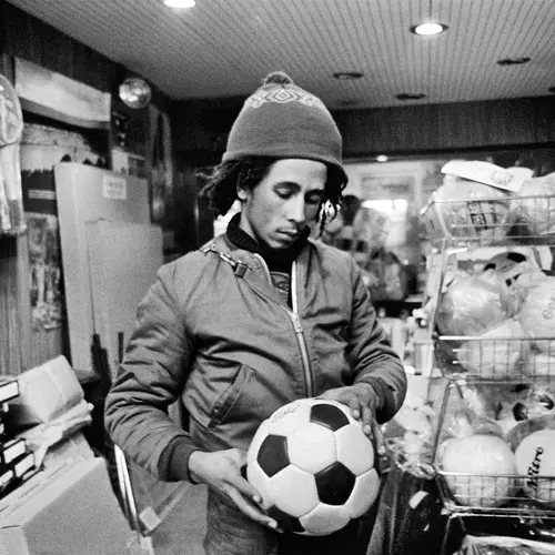 Black and white photograph of Bob Marley holding a football in a sports shop.
