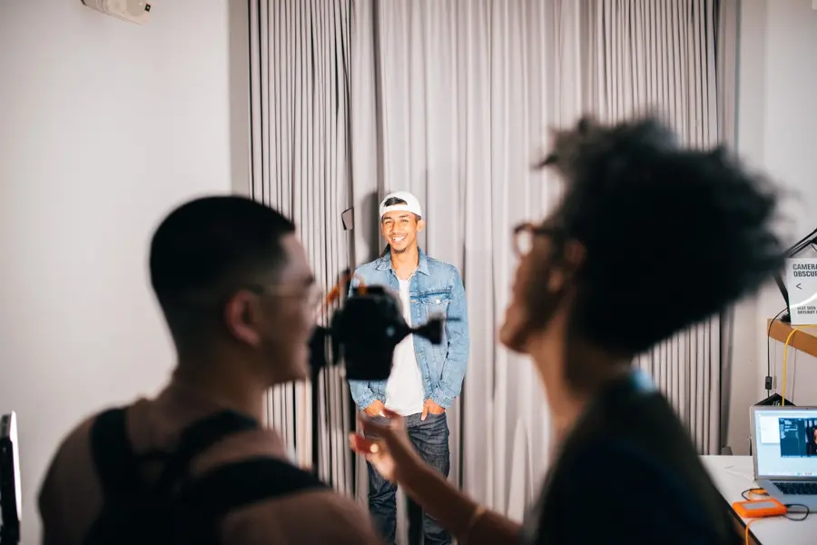 Two people looking at a camera with someone posing in front of it