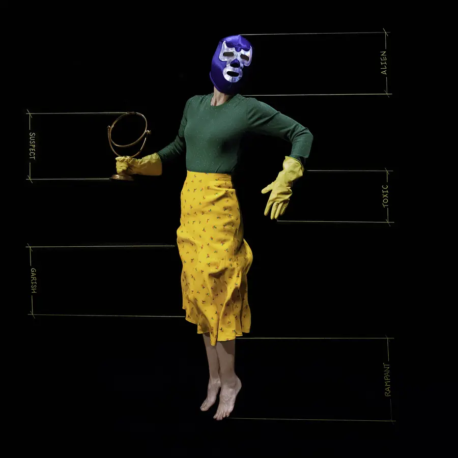 photograph of a woman wearing a blue mask and washing up gloves in front of a black screen by Monica Alcázar-Duarte