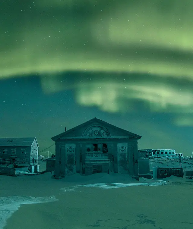 Image of a derelict snowy village with the northern lights in full glory in the sky