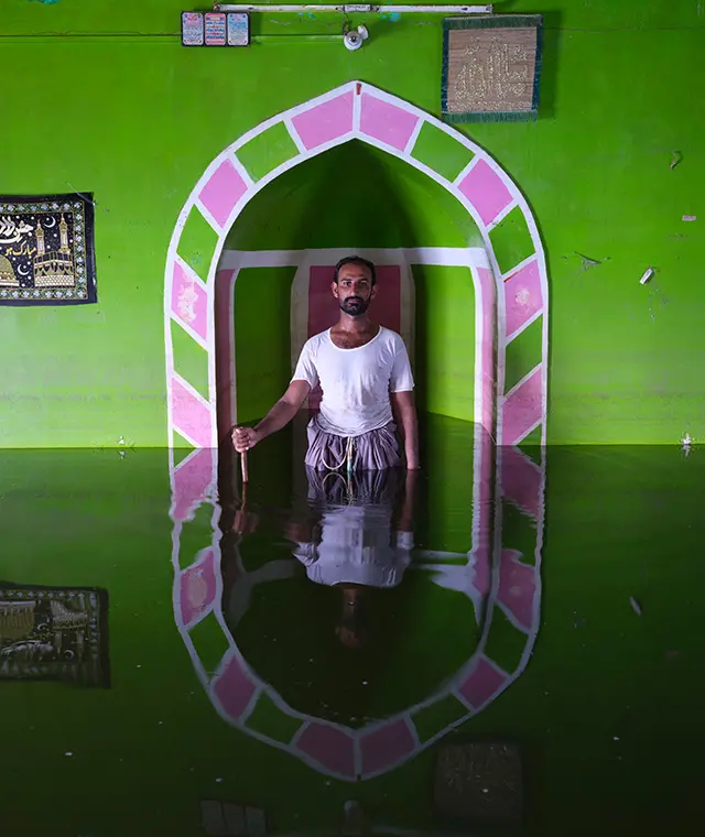 Image of Amjad standing in a doorway in his Pakistan home with floodwaters up to his waist by Gideon Mendel in Soho Photography Quarter.