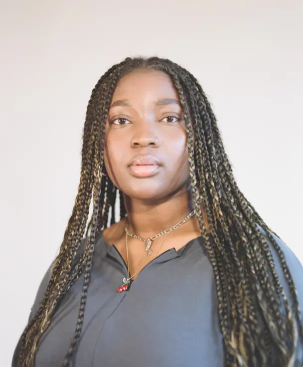 Portrait photograph of a black woman with braids wearing a grey top. 
