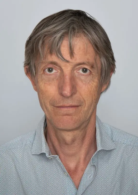 Colour photograph of head and shoulders portrait of a man looking directly at the camera