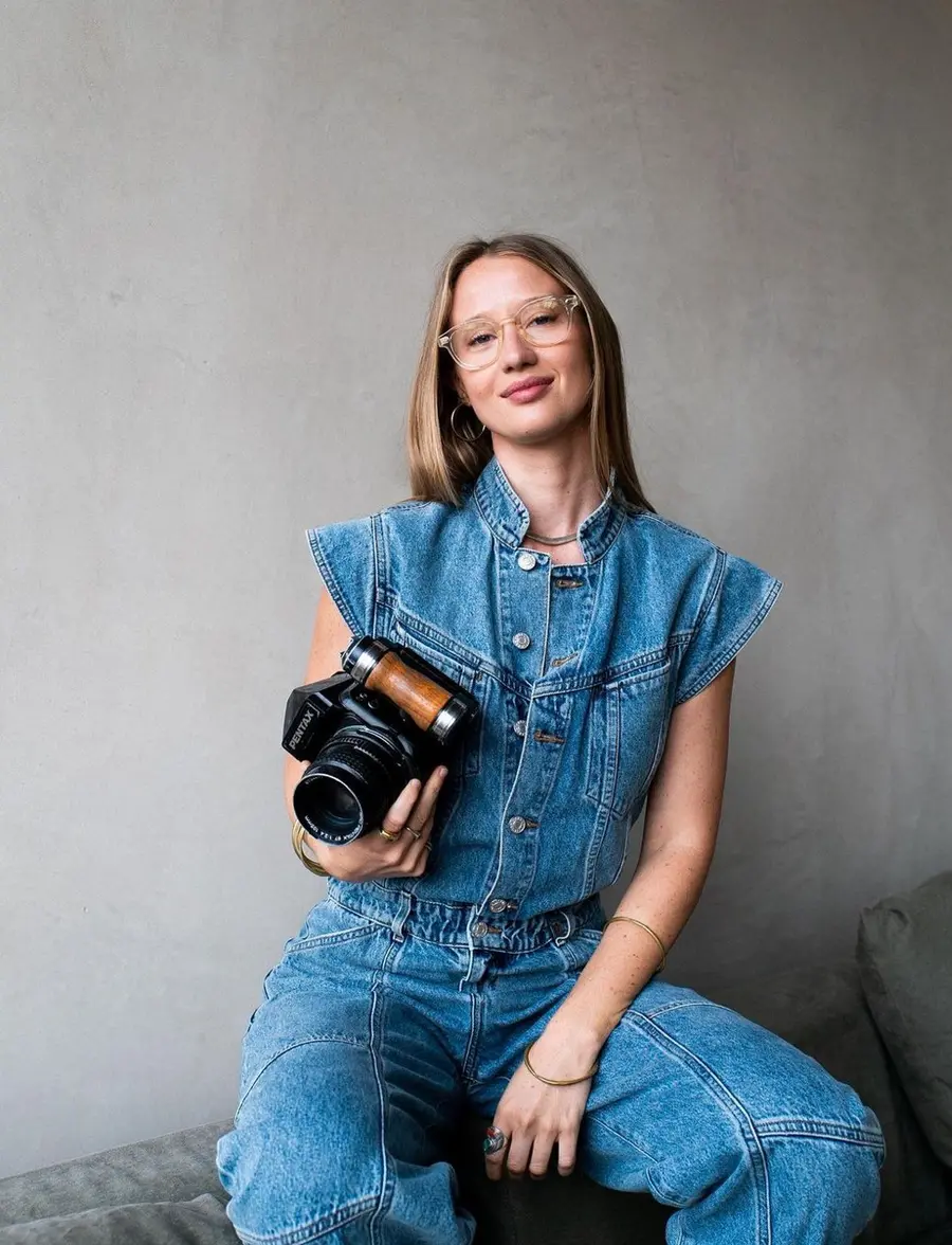 Portrait of Alice Aedy, seated, holding a camera at her waist.