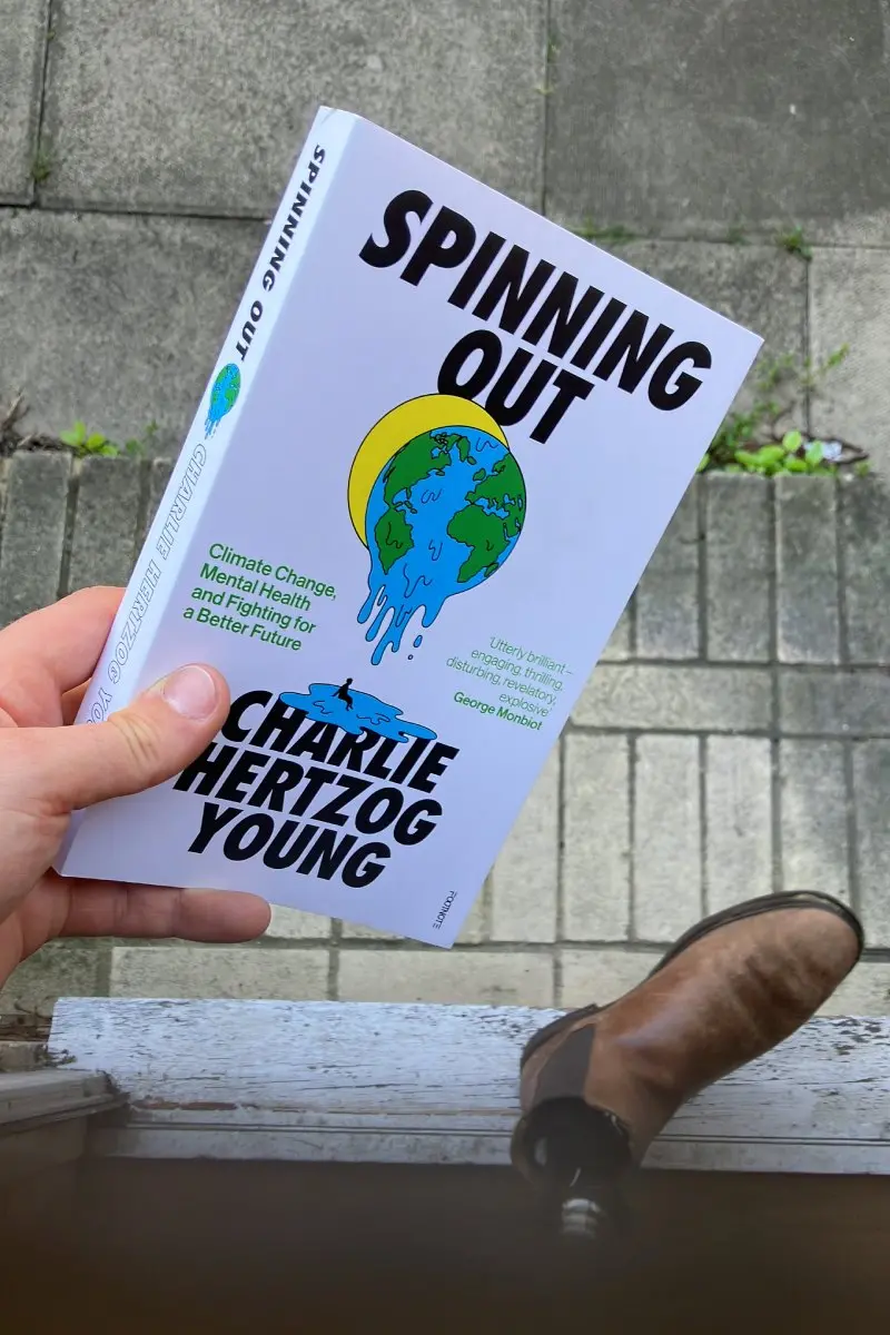 Colour photograph of someone holding a copy of a book titled 'Spinning Out' by Charlie Hertzog Young