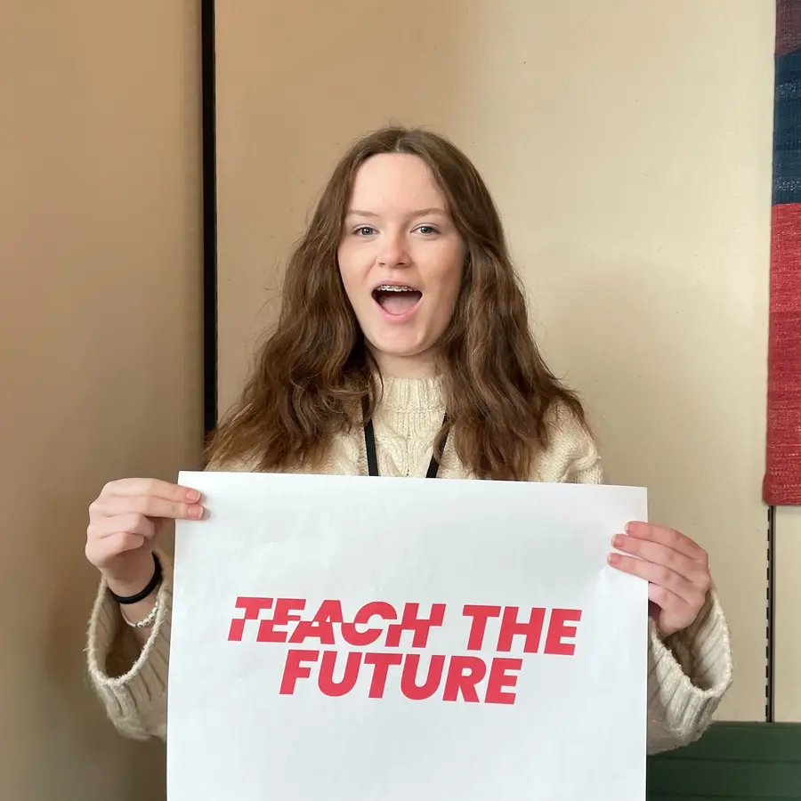 Colour photograph of a person holding a sign with the words Teach the Future