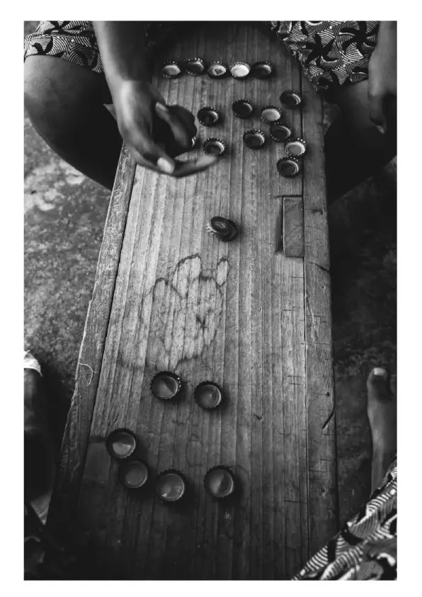 Black and white photograph of an aerial view of a wooden bench with bottle tops being played in a game