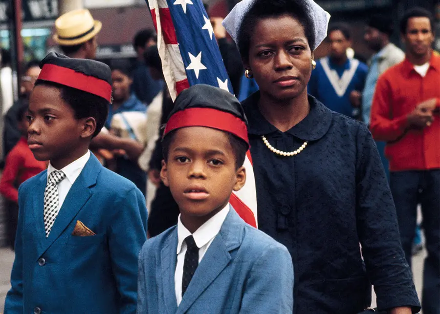 Colour photograph of two children with a woman standing behind them carrying the flag of the United States of America 