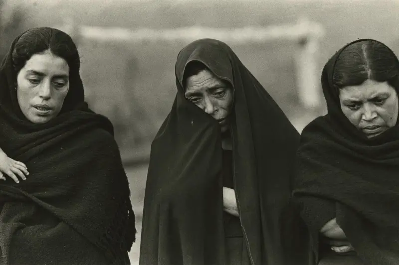 Black and white photograph of three women with black headscarves wrapped around them looking forlorn