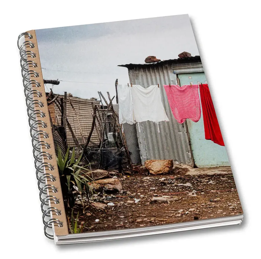 Image of a closed book that features a colour photo of a clothes hung out to dry on a washing line in a street. The street has a dirt road and small corrugated iron buildings. The book has a scrapbook aesthetic.