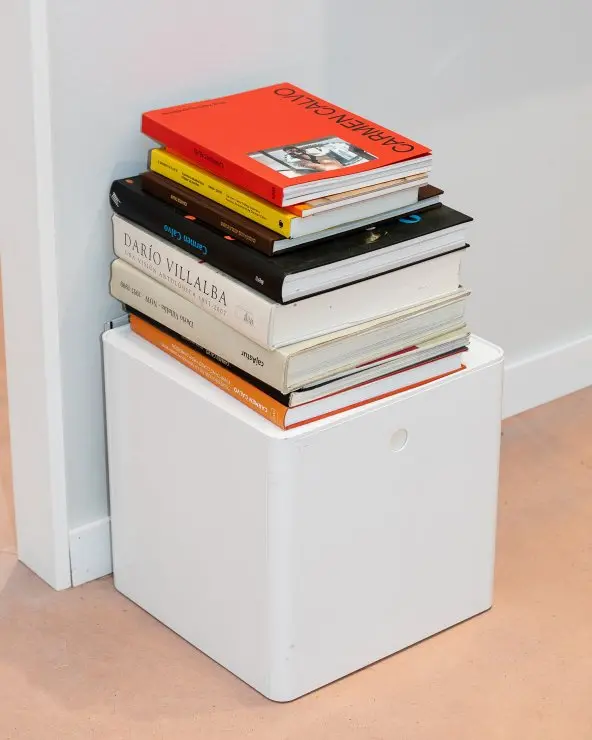 A stack of books piled on top of a white cube.