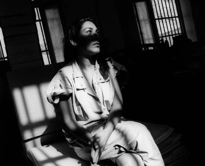 Black and white photograph of a woman sat on a prison bed staring into the distance.