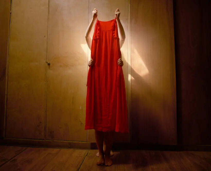 Colour photograph of a two unidentified people holding up a red dress.