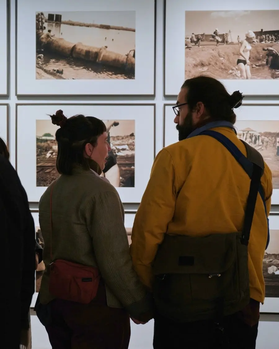 Two people hold hands and look at a display of framed photographs in an exhibition space.