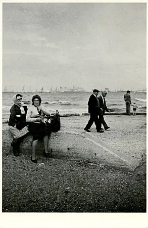 A black and white photo of beachgoers strolling along the coast.