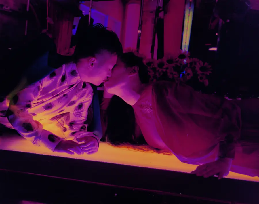 two people lean over a orange-lit counter to kiss each other 