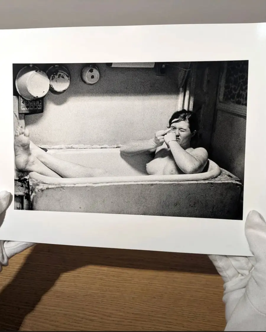 gloved hands hold a photographic print of a woman in a bathtub