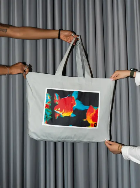 A pair of hands holding up a white tote bag with an image of a fish on the front.