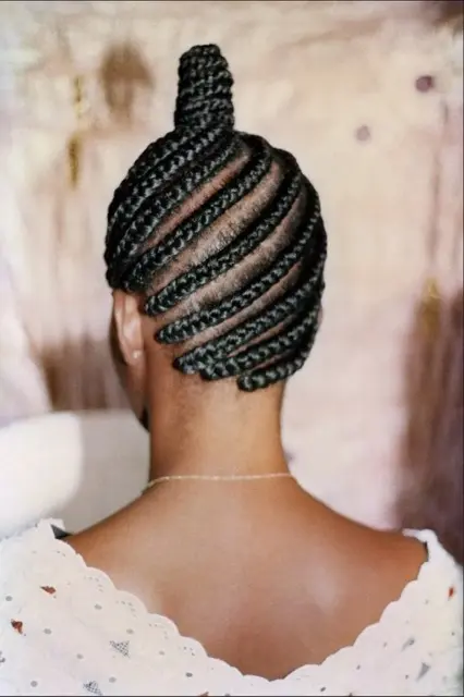 A view of a the back of a woman's head who has cornrows and braids gathered into a bun on the top of her head.