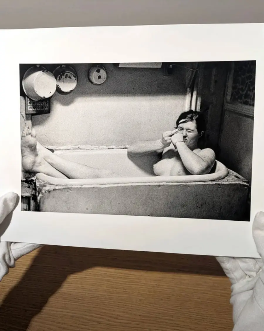 A pair of gloved hands holding up a black and white print of a person in the bath.