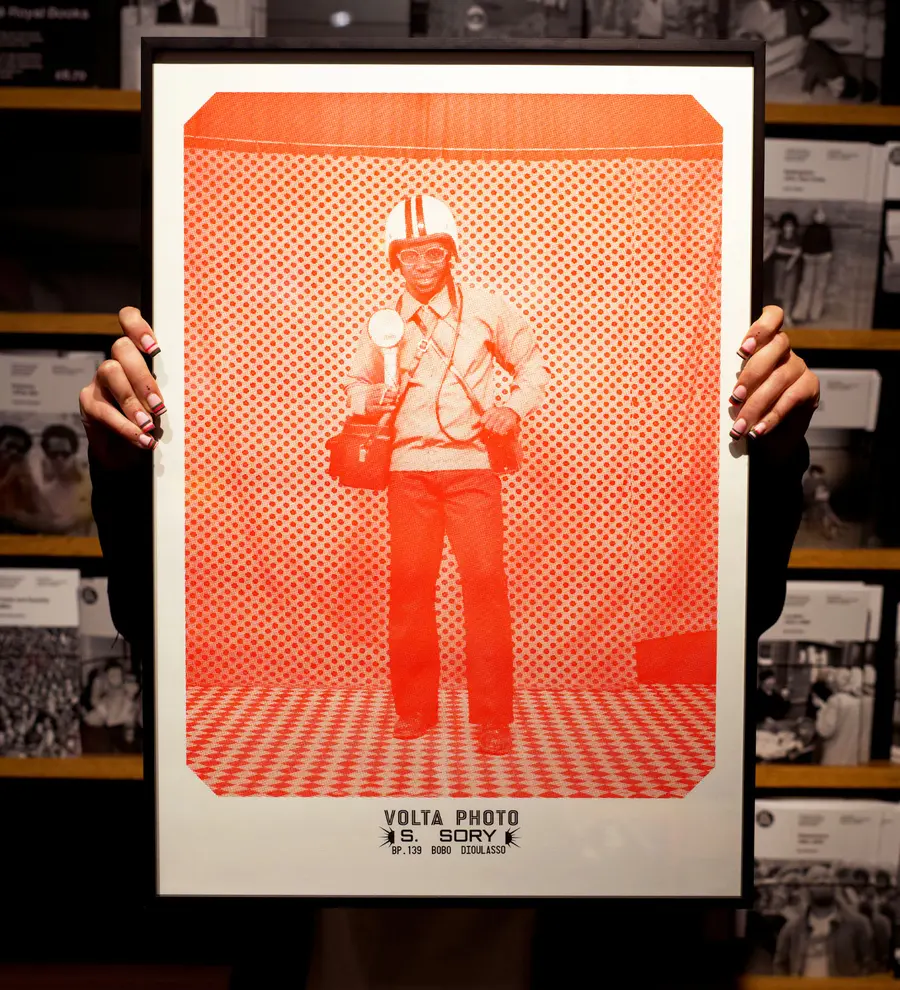 A risograph print showing a photographer looking at the camera. Two hands are holding the print up