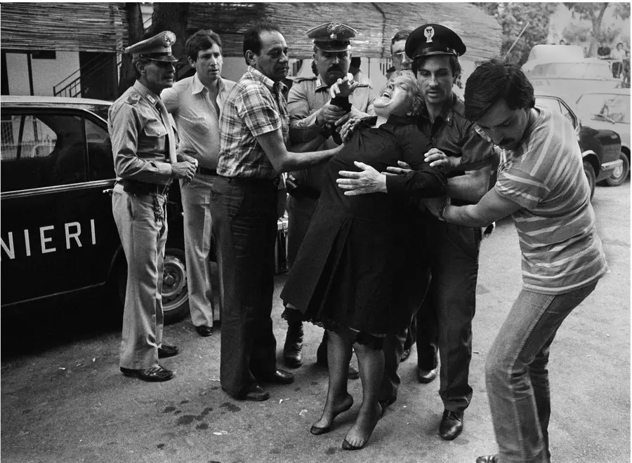 A women who is grieving is being held up as she flops into the arms of a group of men and policemen. She is visibly distressed.