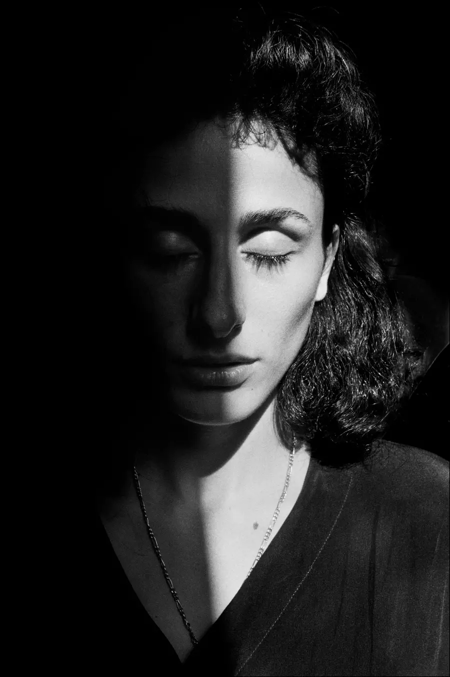 Black and white photograph of a woman with her eyes closed. She appears to be partially covered by a shadow.